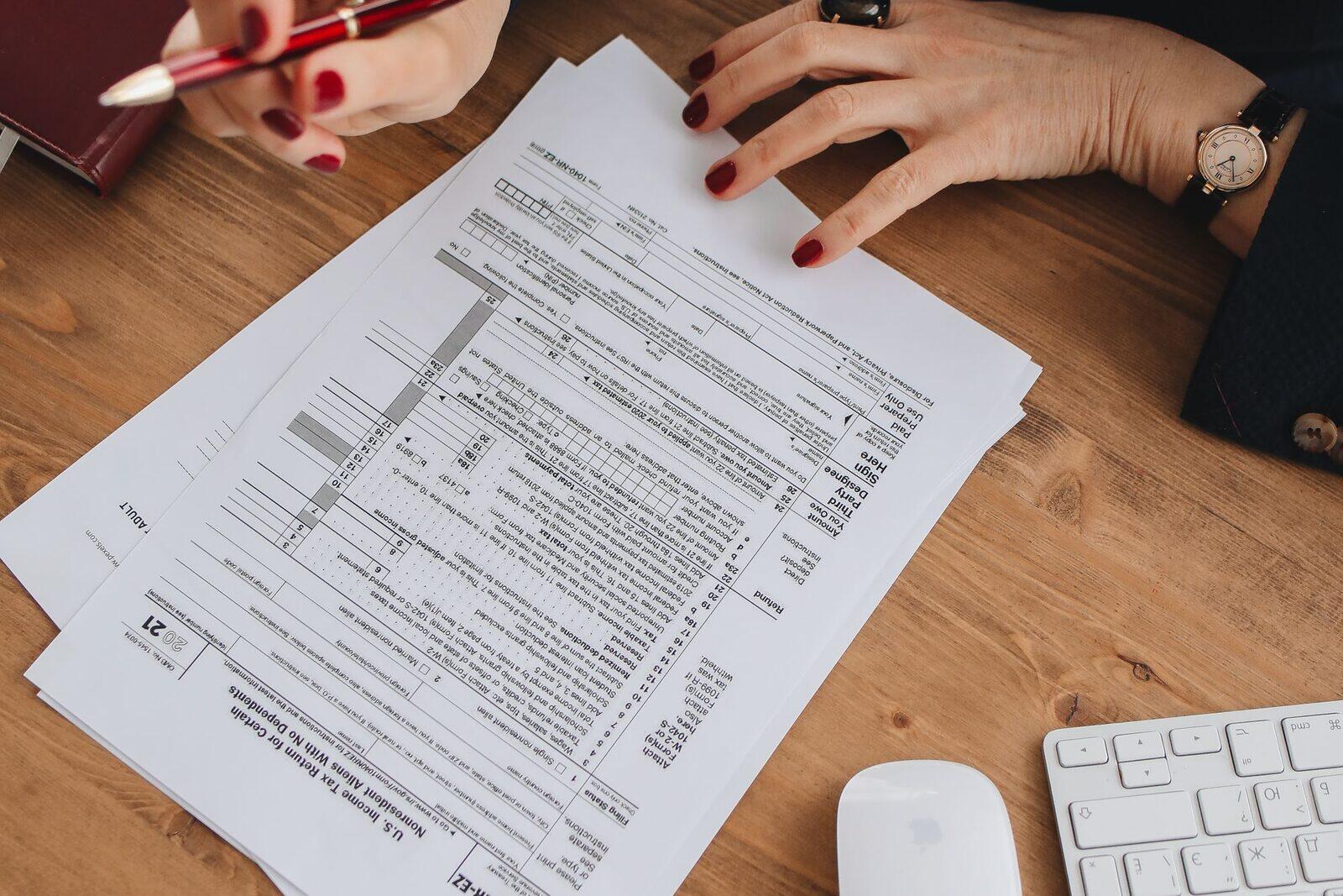 Mains annotant une liasse fiscale sur un bureau en bois, clavier posé à côté