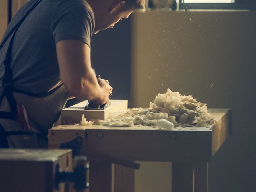 Artisan rabotant une pièce de bois dans son atelier, copeaux en suspension