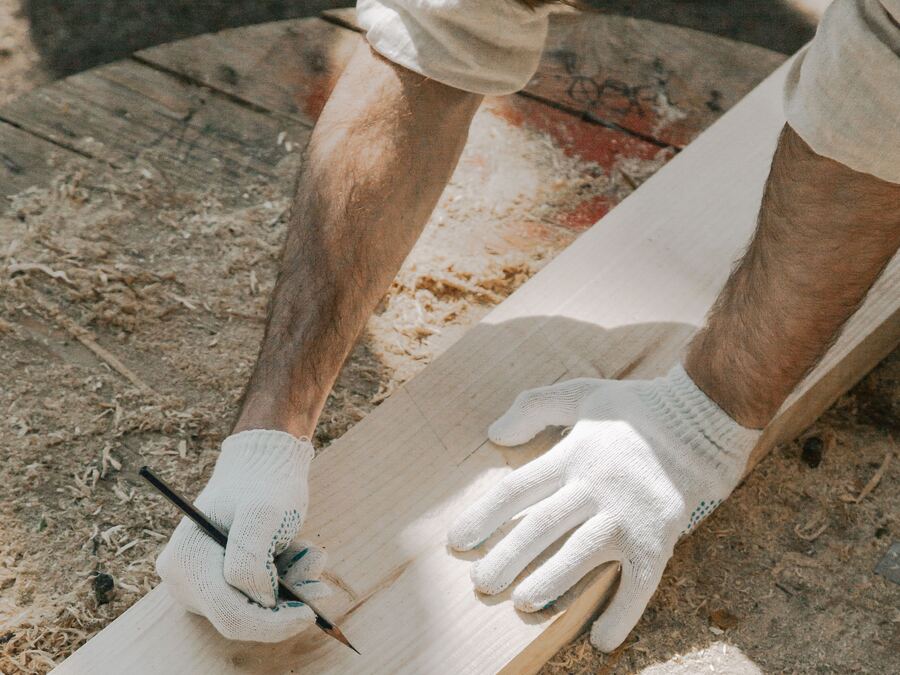 Mains gantées sciant une planche, boîte à outils posée au sol
