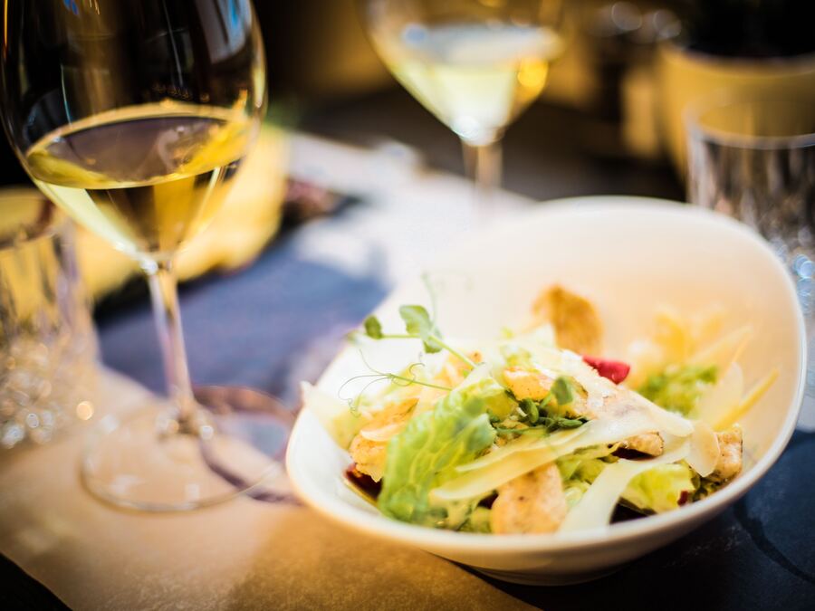 Salade servie dans un bol blanc, verres de vin en arrière-plan