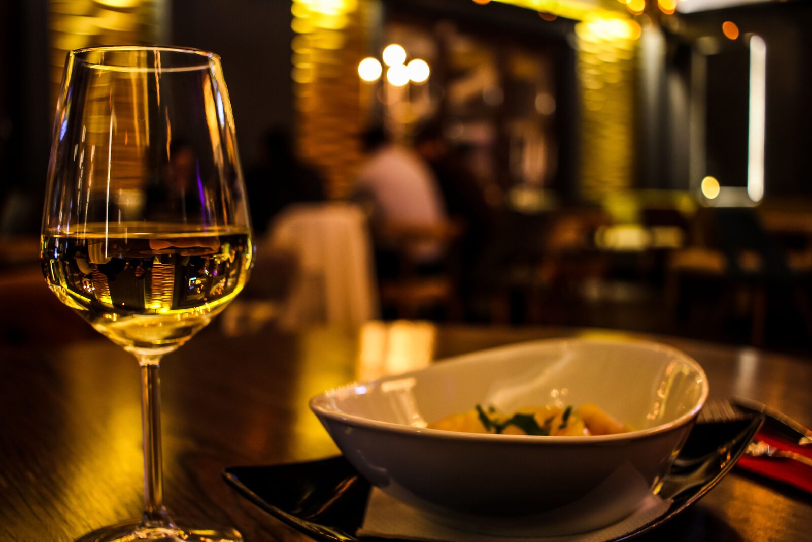 Verre de vin blanc et assiette dressée dans une salle de restaurant tamisée